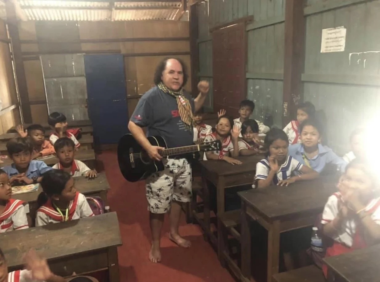 James Garcia playing guitar for children in a classroom in Kampong Thmorr.