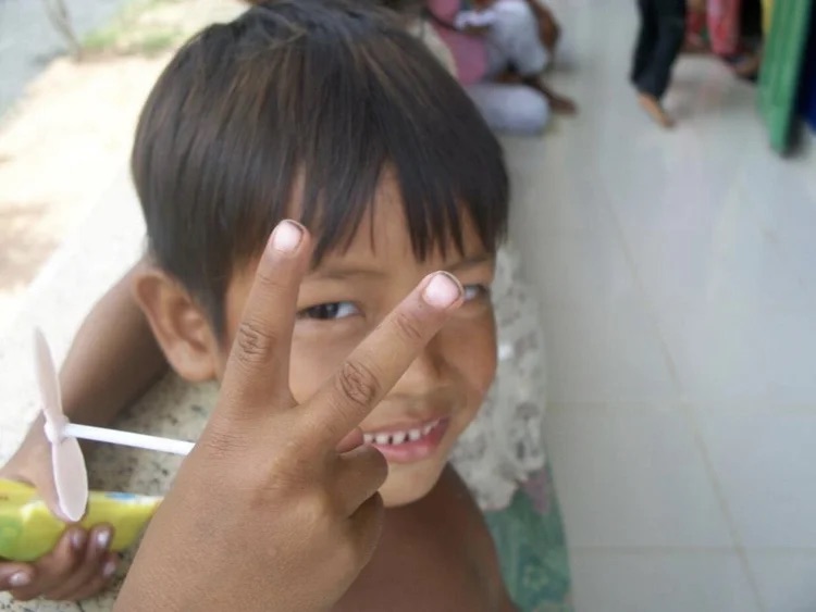 A smiling child holding a pinwheel and making a peace sign.