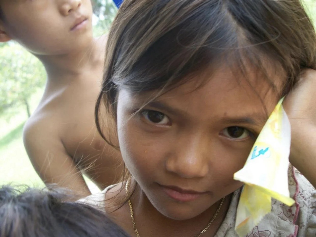 A young Cambodian girl looking toward the camera, holding a paper kite.