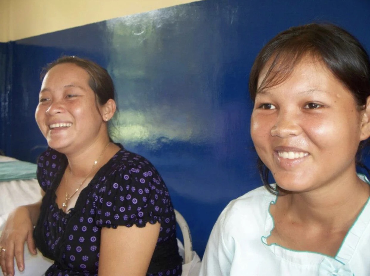 Two Cambodian women smiling and laughing together indoors.