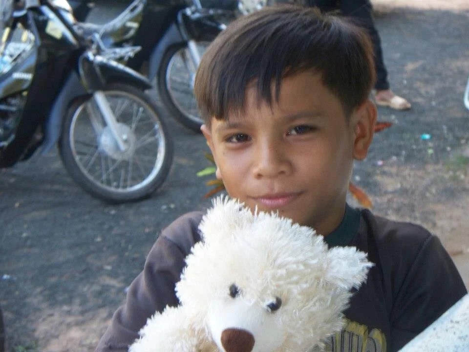 A boy holding a white teddy bear on a village road.